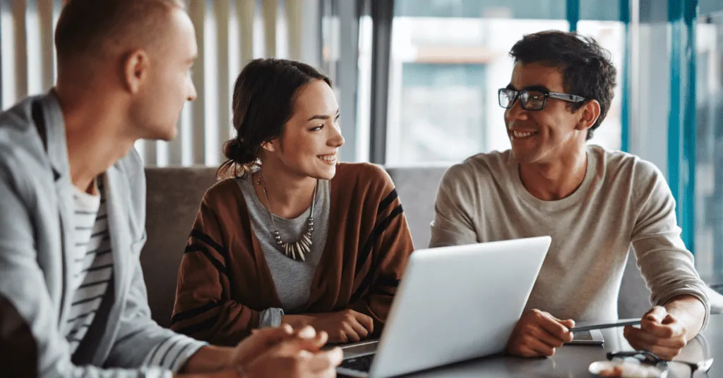 Team members communicating around a laptop showcasing The Benefits of Team Building Activities in 2022