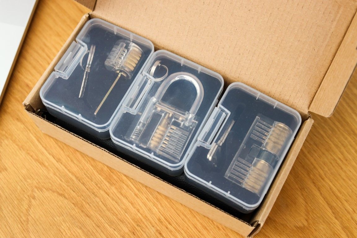 An open shipping box holding three transparent practice locks in clear cases