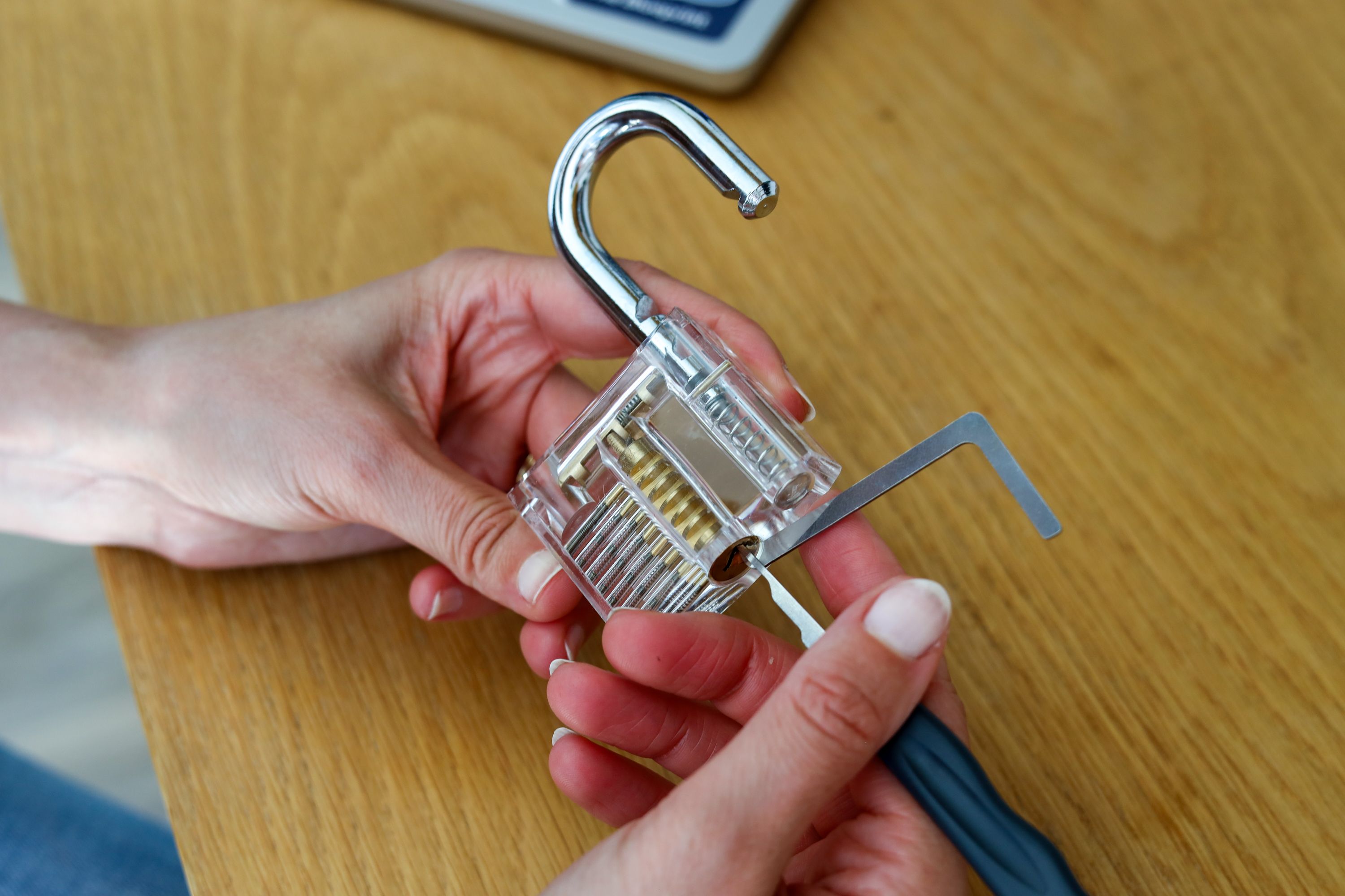 Hands holding a transparent lock cylinder with a pick and tension wrench inserted