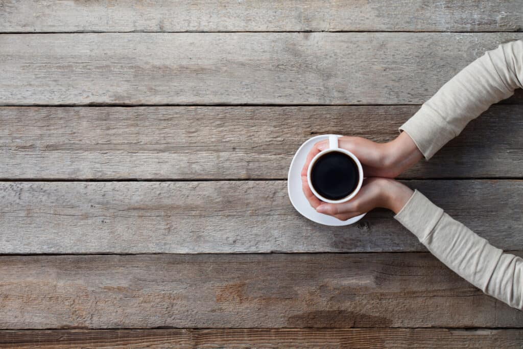 woman hands holding mug of hot coffe cup that standing on wooden table