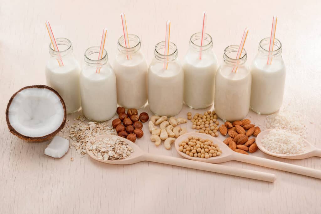 Bottles of assorted plant milk and ingredients on beige table. Organic drinks for vegans and lactose-intolerant people.